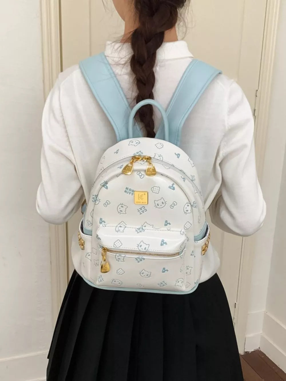 Playful mini backpack with cat print and light blue straps, gold hardware.