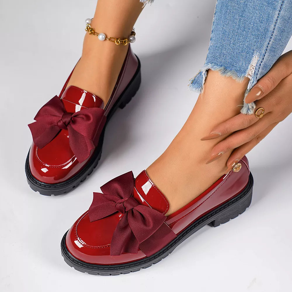 Burgundy patent loafers with large satin bows, featuring a chunky sole.