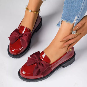Burgundy patent loafers with large satin bows, featuring a chunky sole.