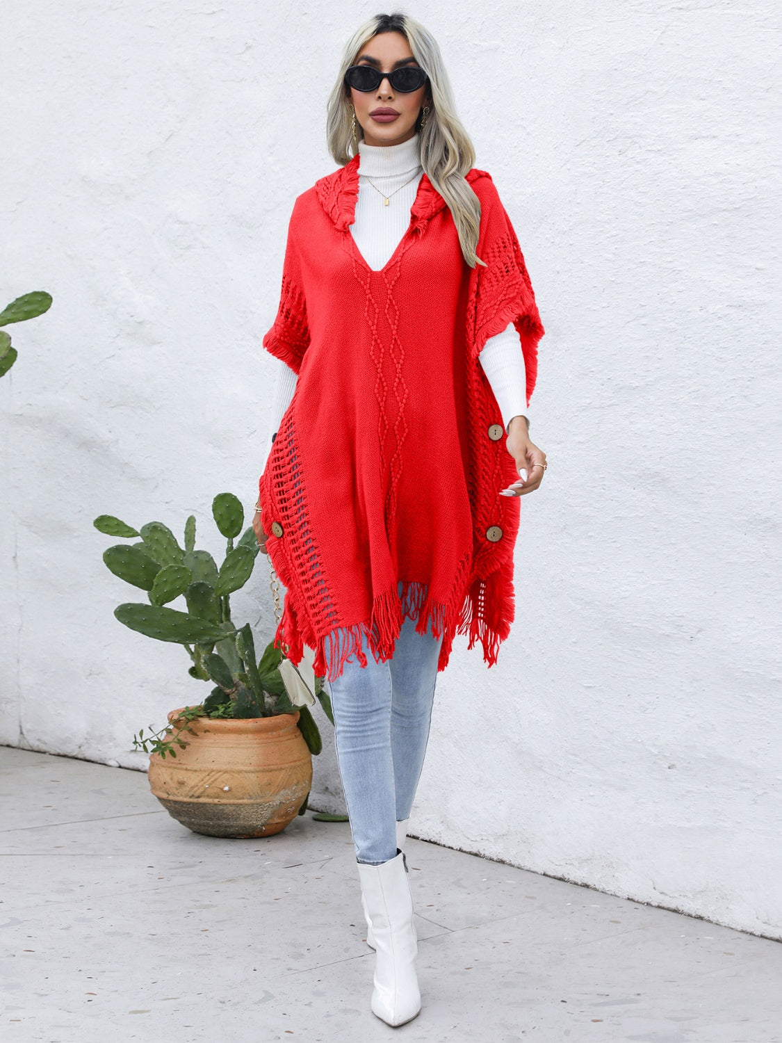 Red knit poncho with fringe, wooden buttons, and textured pattern.