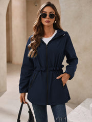 Navy hooded windbreaker jacket with ruffled waistline and zippered pockets.