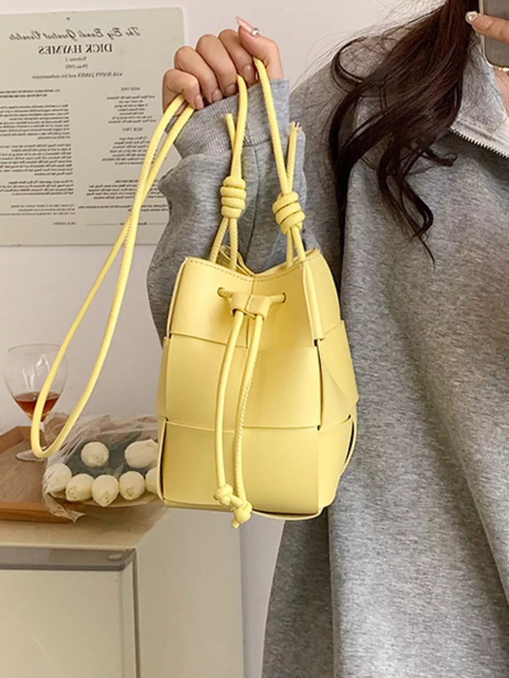 Yellow woven mini bucket bag with drawstring closure and knotted straps.