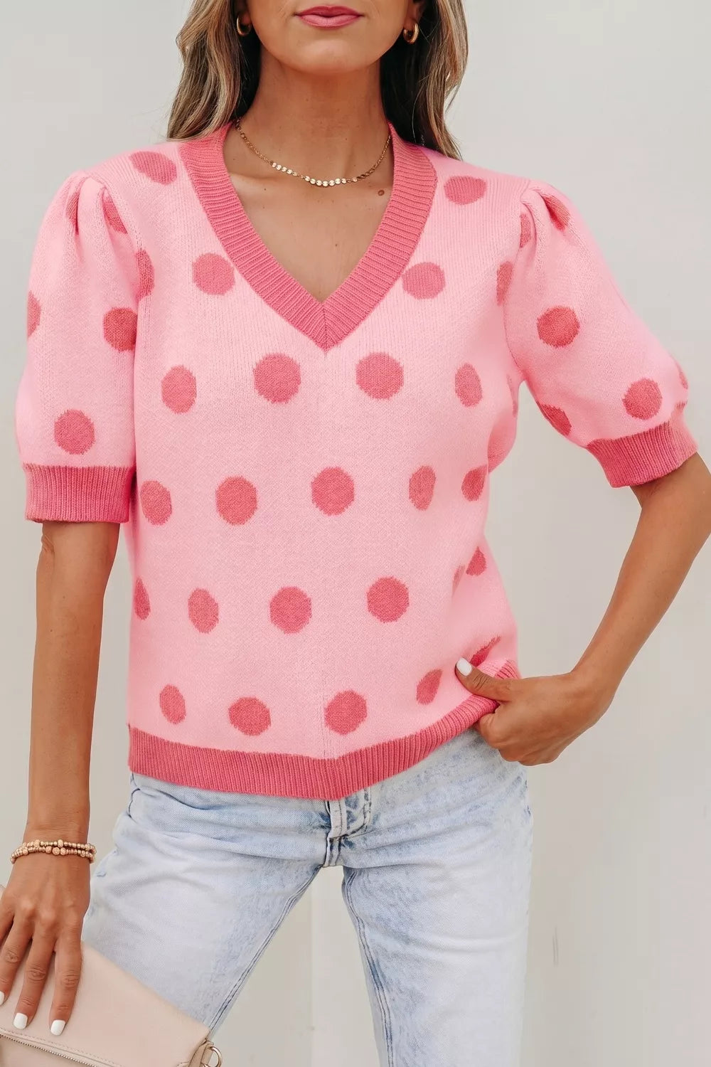 Pink polka dot knit top with V-neck, puff sleeves, and contrast trim.