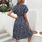 Dark blue midi dress with white dots, short sleeves, belted waist, and pleated skirt.