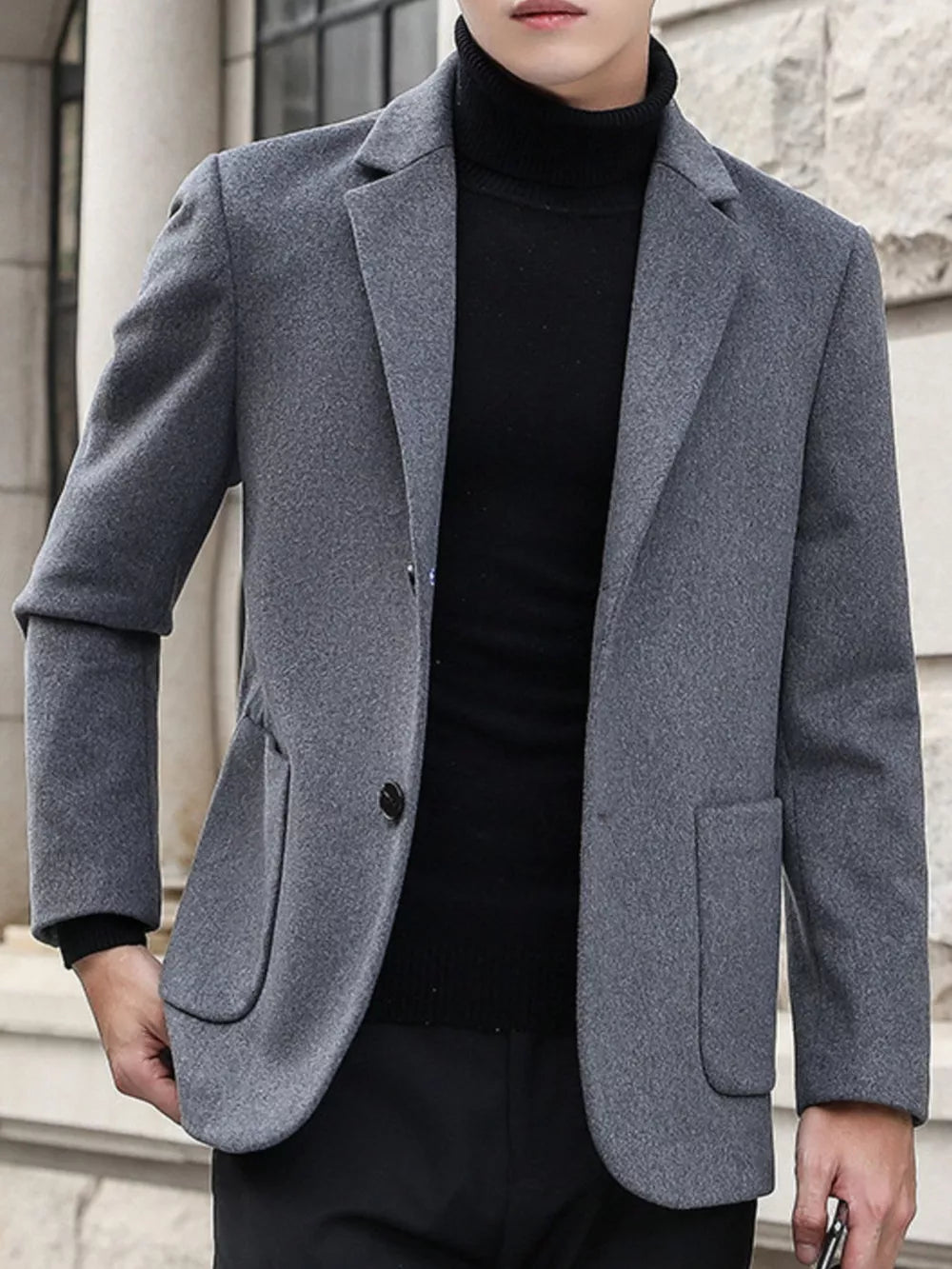 Men's grey lapel collar blazer with button closure and flap pockets, styled with a black turtleneck.