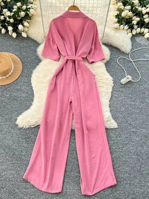 Pink belted wide-leg maternity jumpsuit with pockets and short sleeves.