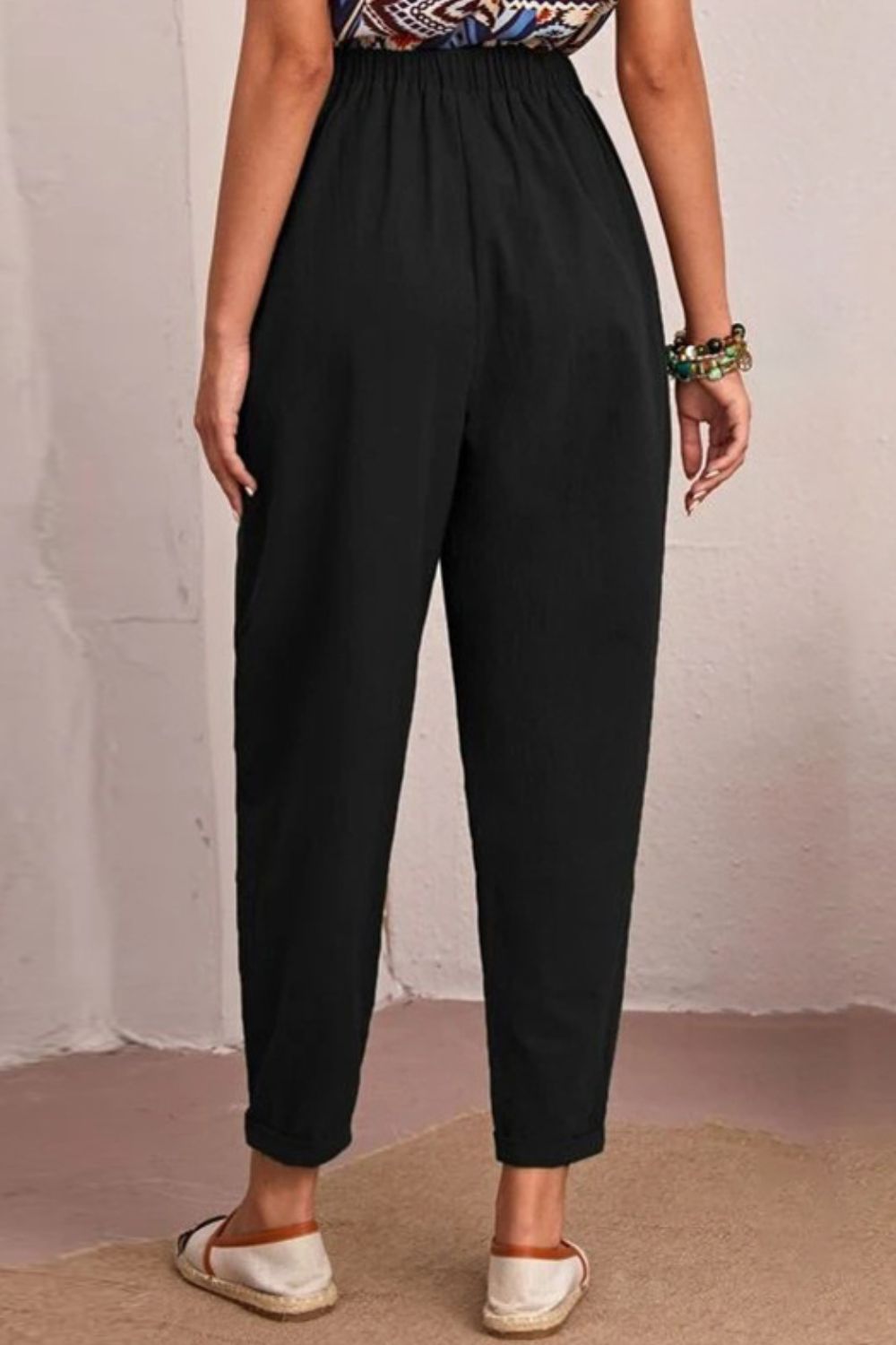 Black linen tapered trousers with elastic waist and cuffed hem.