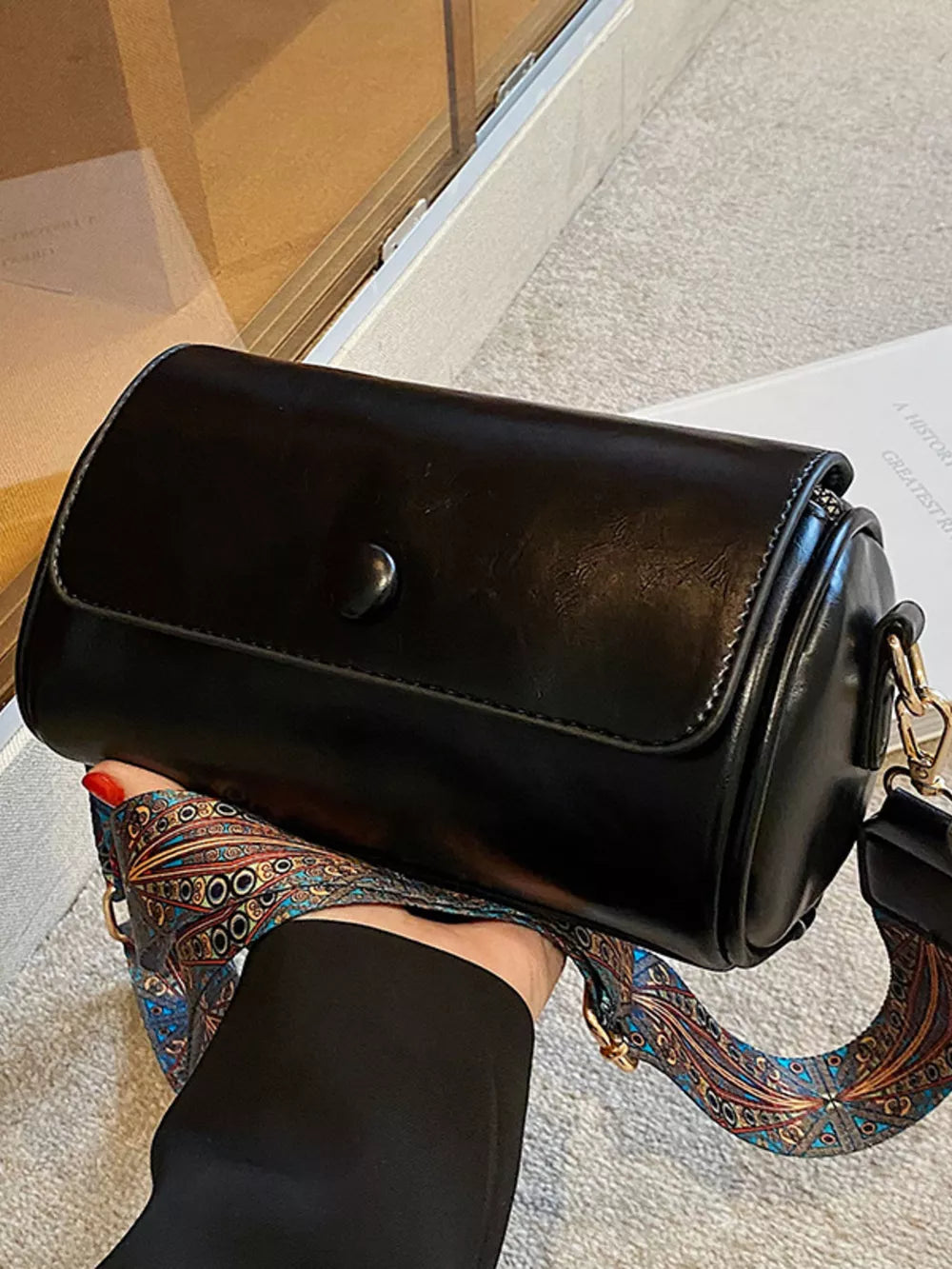 Black leather mini crossbody bag with a colorful ethnic print strap.