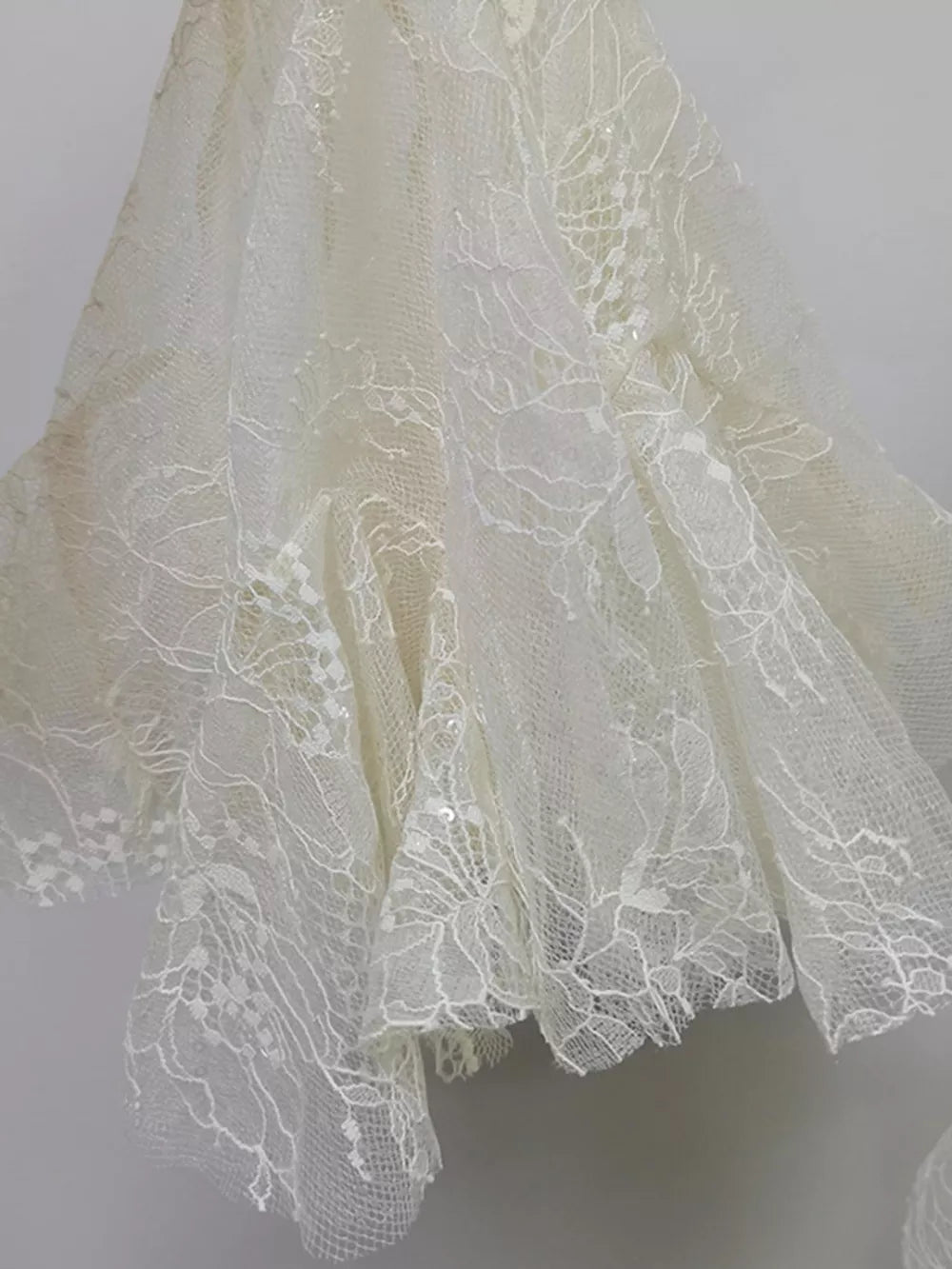 White floral lace dress detail with ruffle hem and subtle sequins.
