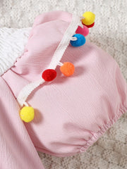 Blush pink cotton one-piece with smocked white top and pom-pom trim.
