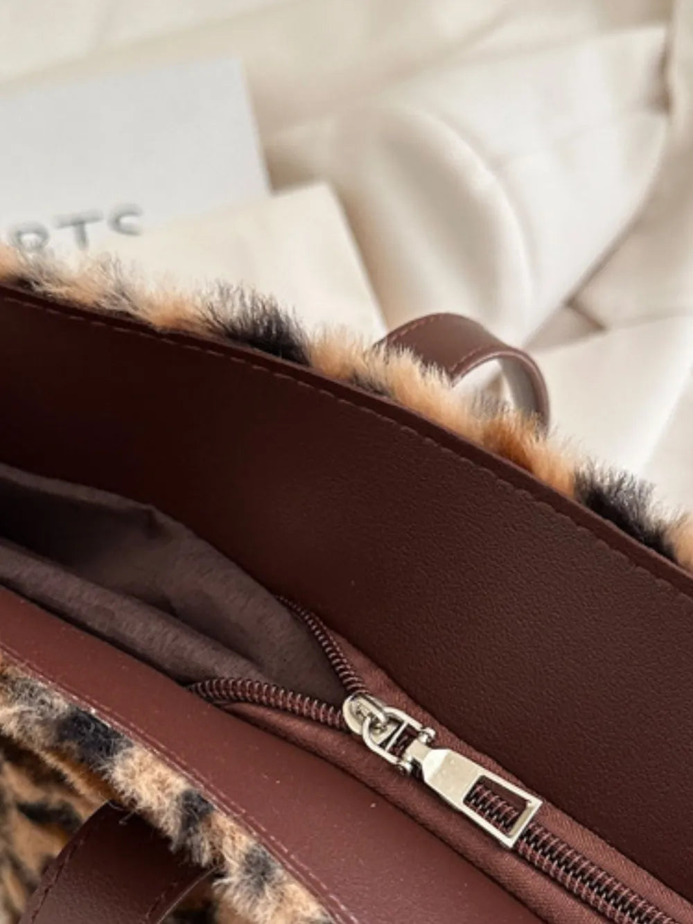 Fuzzy leopard print tote bag with brown faux leather trim and zipper detail.