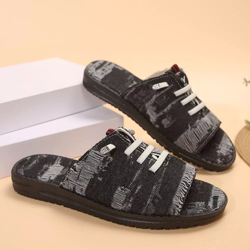 Black canvas slide sandals with distressed pattern and white lace detail.