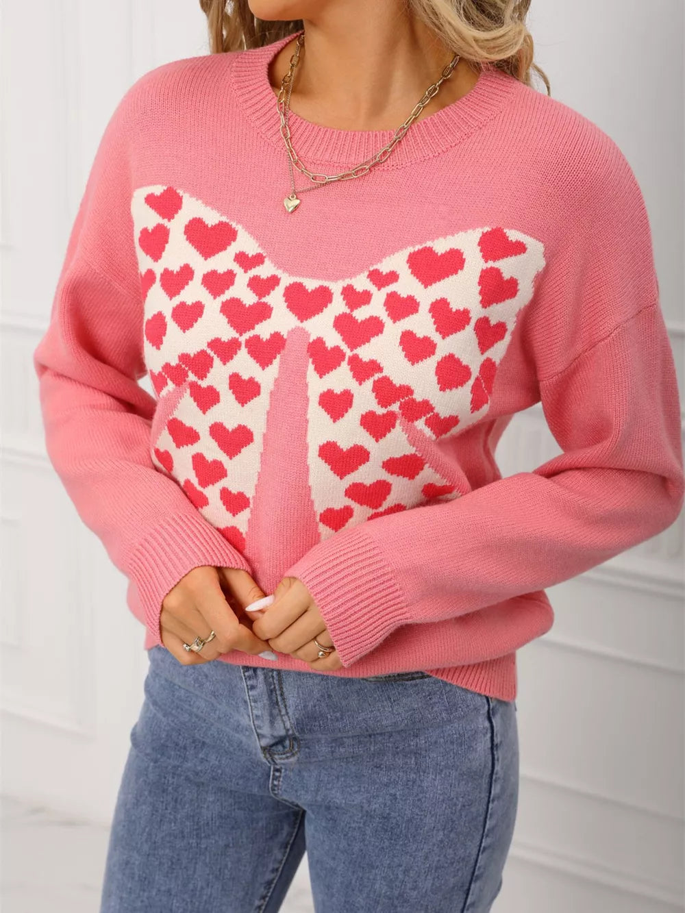 Pink acrylic knit sweater with heart bow detail and round neck.