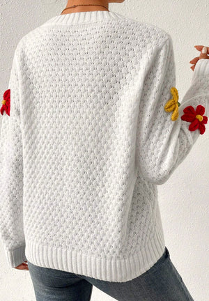 White knit sweater with crochet floral embellishments on sleeves.