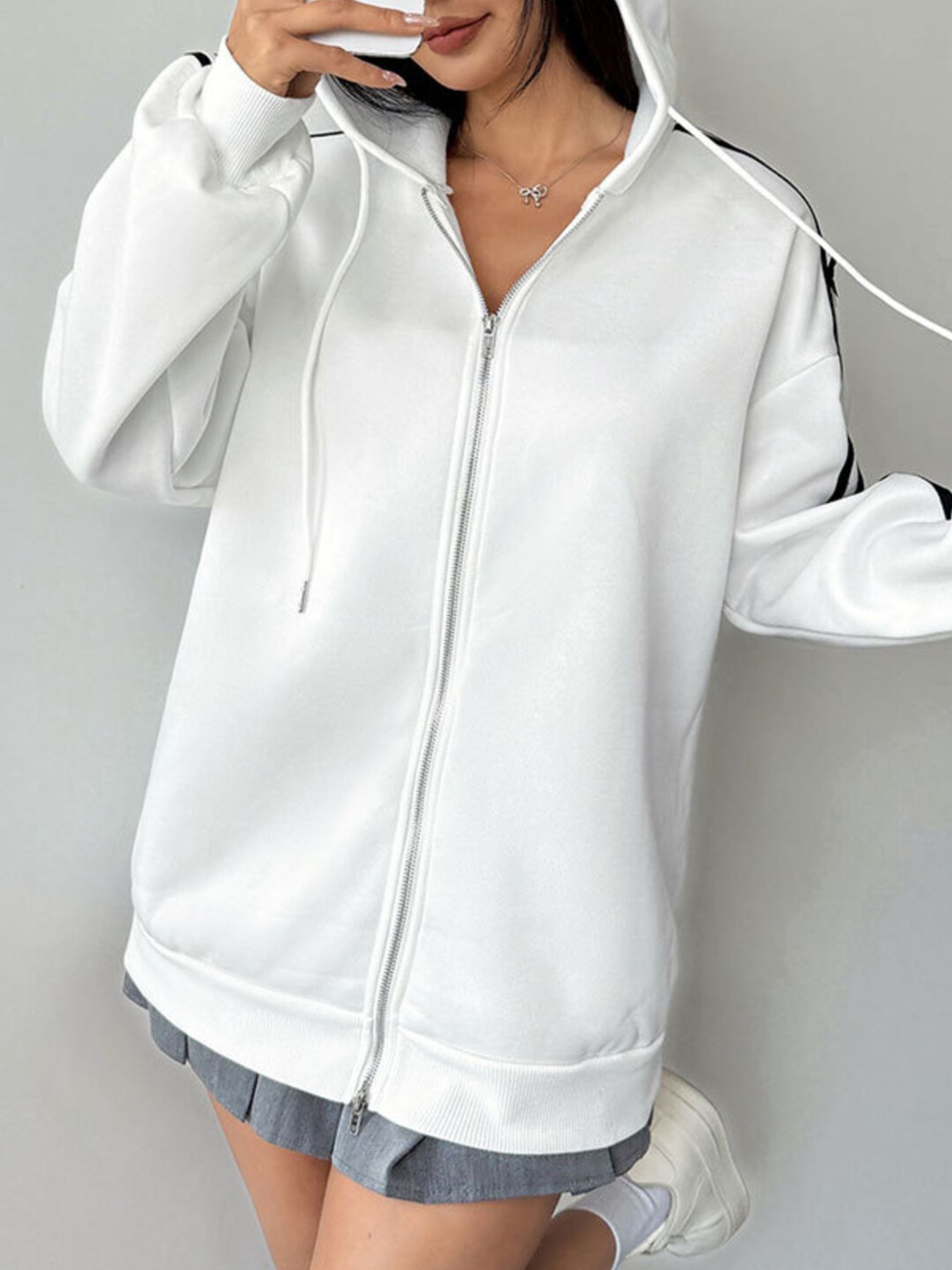 White zip-up hoodie with black stripes on sleeves and drawstring hood.