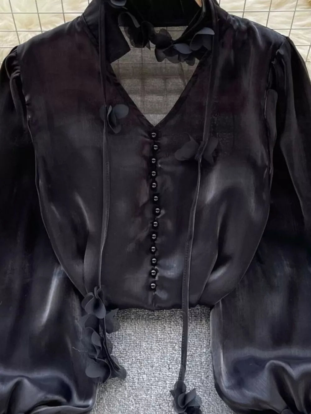 Black button-down shirt with delicate floral appliqué and tie neck detail.