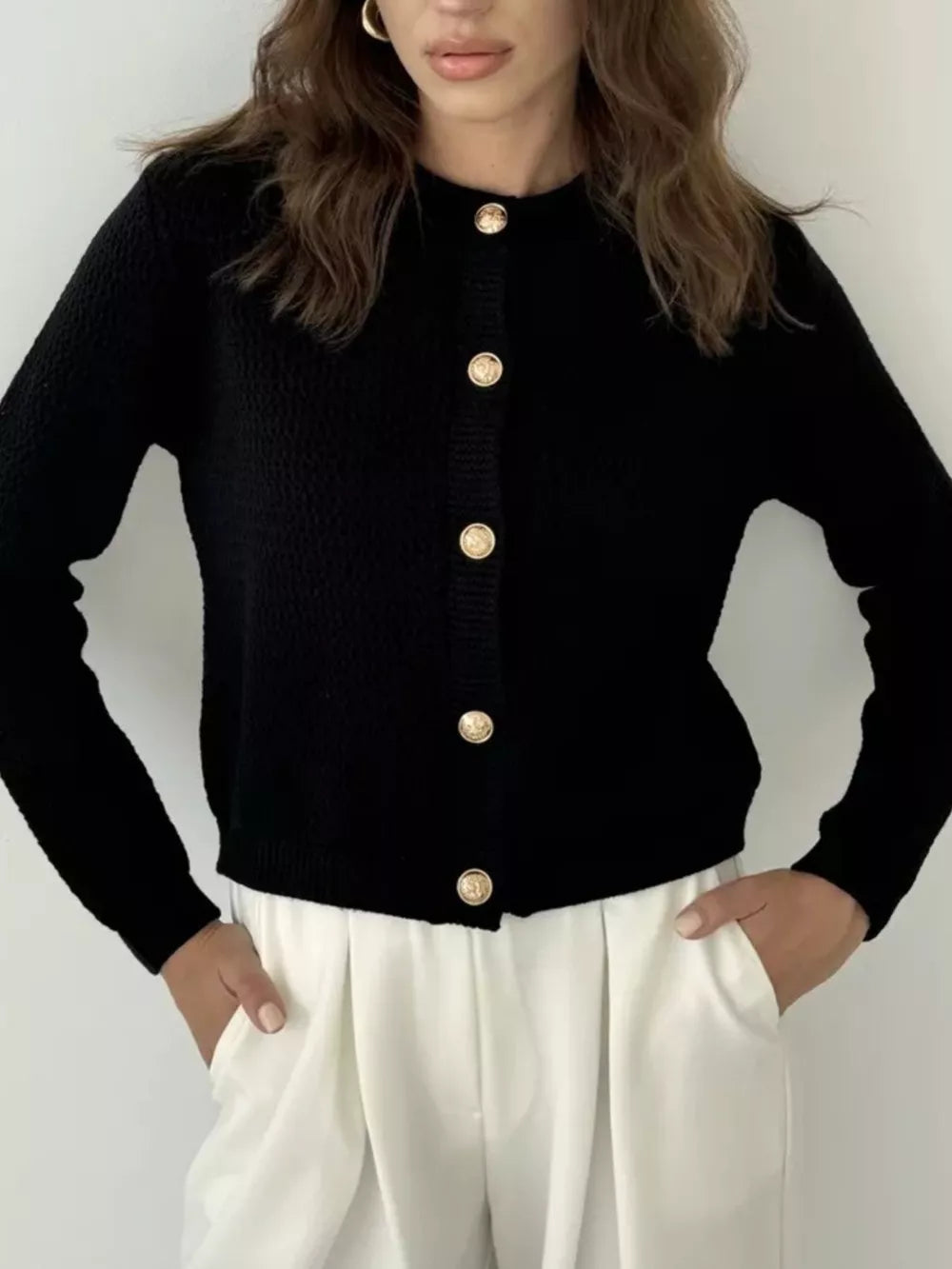 Black textured knit cardigan with round neckline and elegant gold button detail.