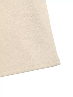 Cream pleated V-neck strapless romper detail showing textured fabric and hem.