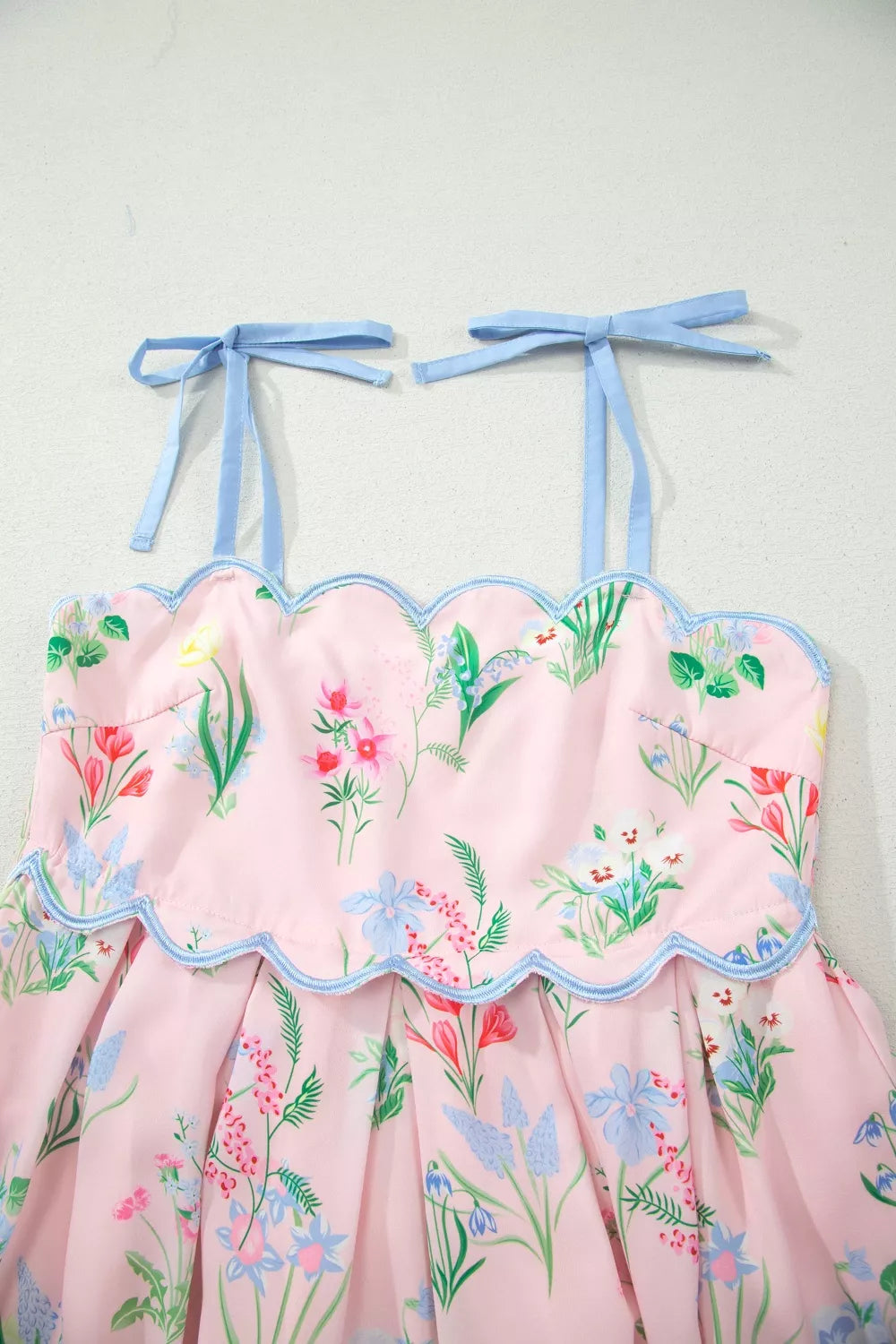 Pink midi dress with wildflower print, scalloped trim, and blue tie straps.