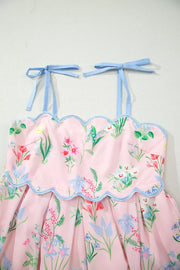 Pink midi dress with wildflower print, scalloped trim, and blue tie straps.
