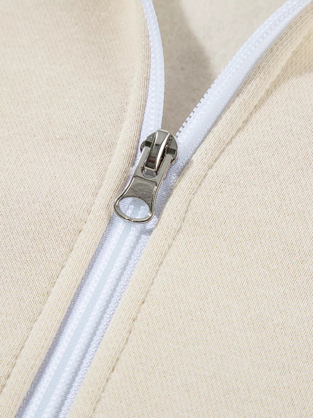 Beige cotton zip-up jacket detail with silver zipper pull and white zipper tape.