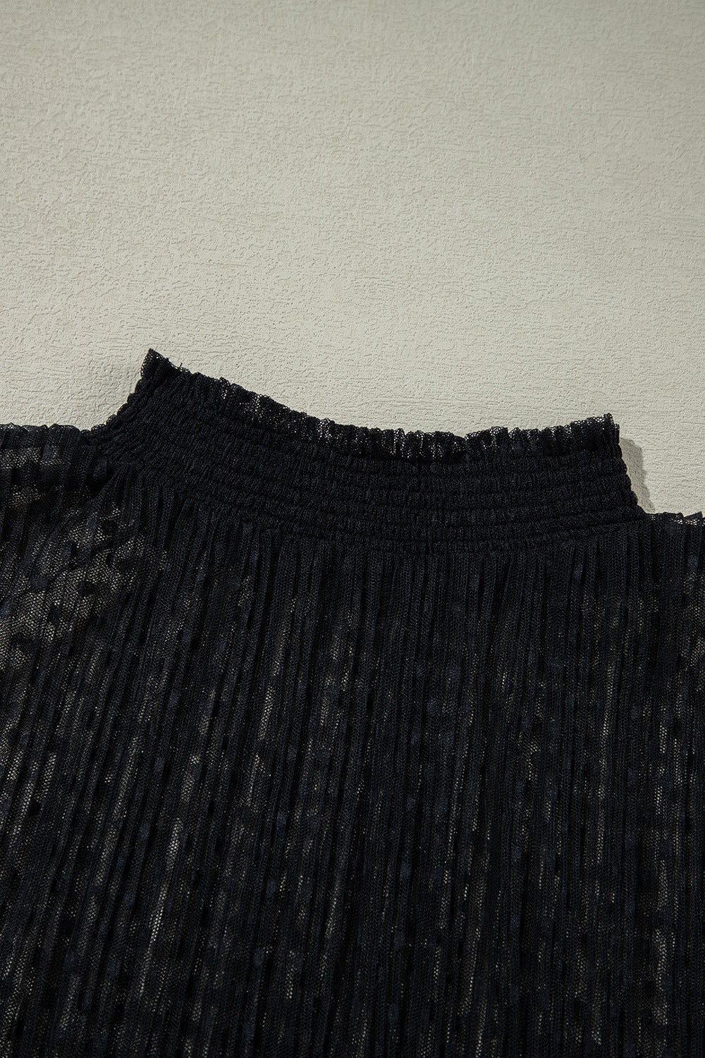 Black sheer mock neck blouse with textured dots and smocked neckline.