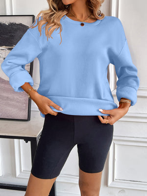 Light blue relaxed fit sweatshirt with crew neck and cuffed sleeves, shown with black biker shorts.