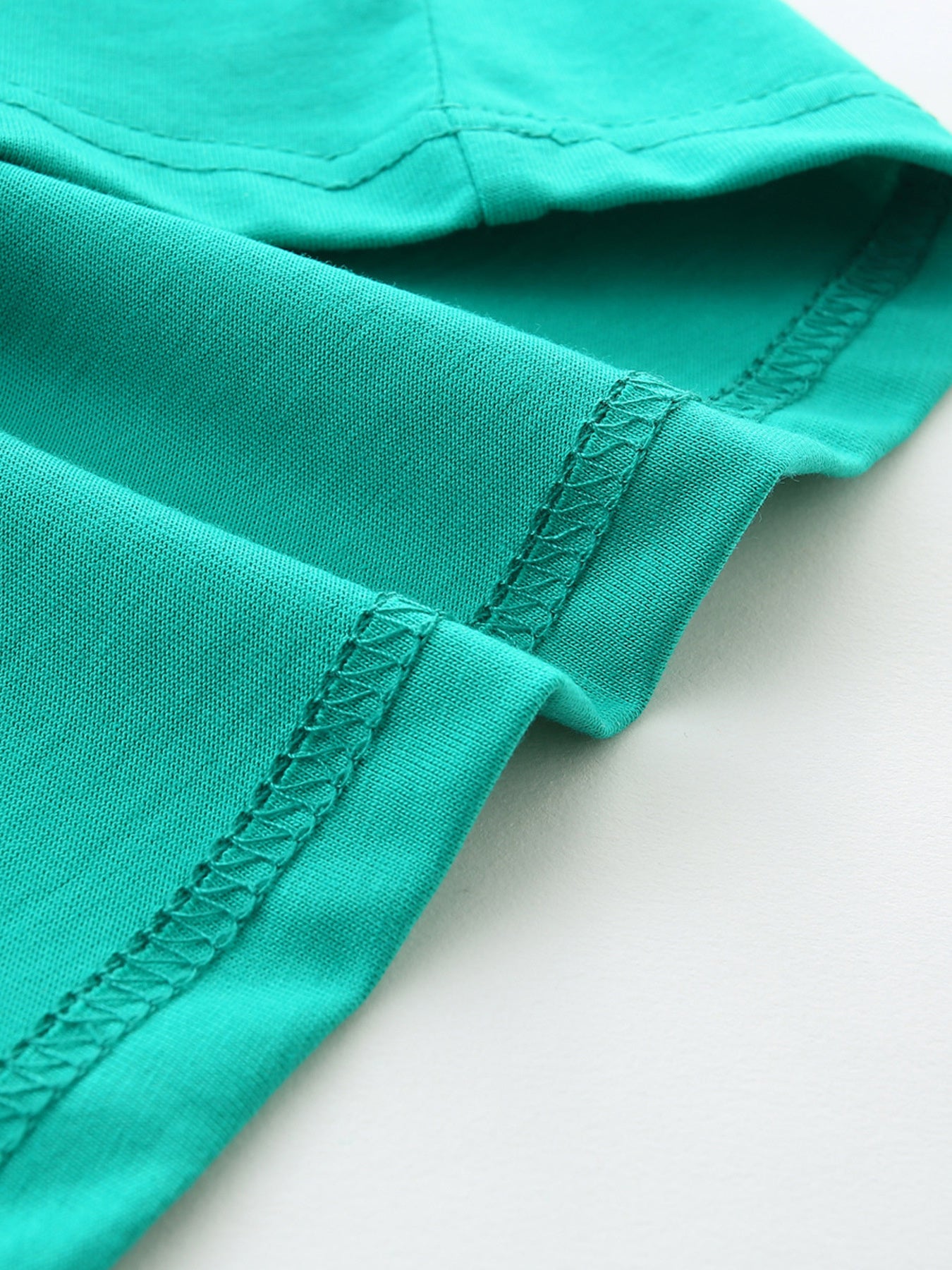 Teal cotton t-shirt detail showing crew neck and short sleeve seam with zigzag stitching.