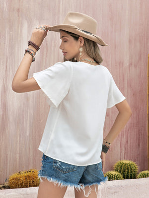 White embroidered medallion blouse with flutter sleeves and a V-neckline.