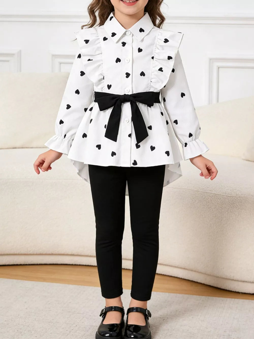 White button-down shirt with black heart print, ruffles, and bow belt, paired with black leggings.