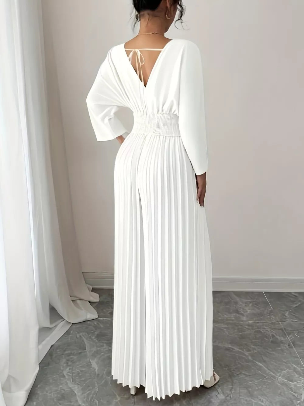 White pleated wide-leg jumpsuit with cinched waist and tie-back detail.