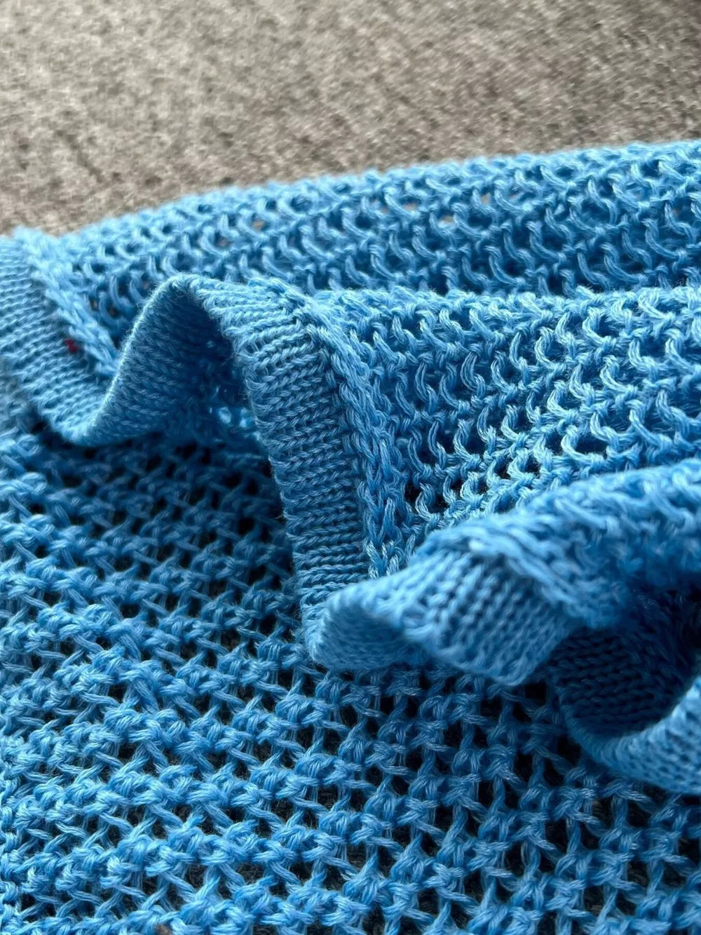 Blue knit crop top with cutout detail and ruffled edge.