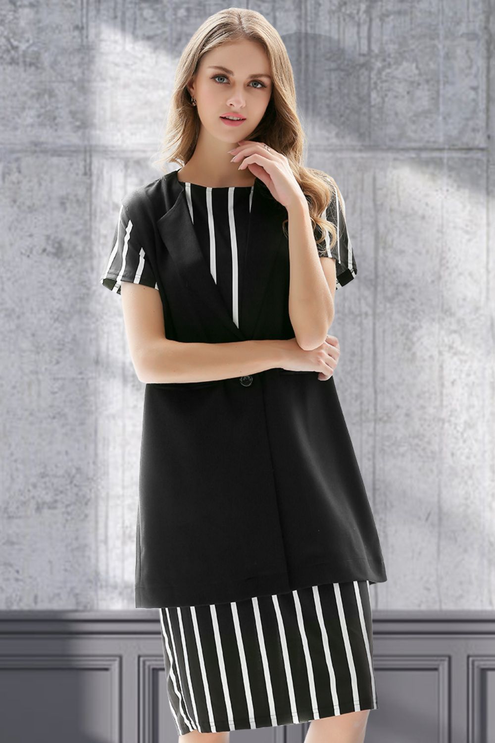 Black sleeveless vest with single button and striped cap sleeves, styled over a striped dress.