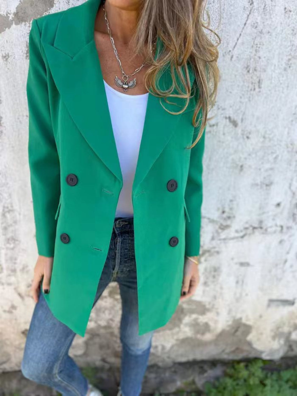 Green double-breasted blazer with sculpted lapels and dark buttons, styled with jeans.
