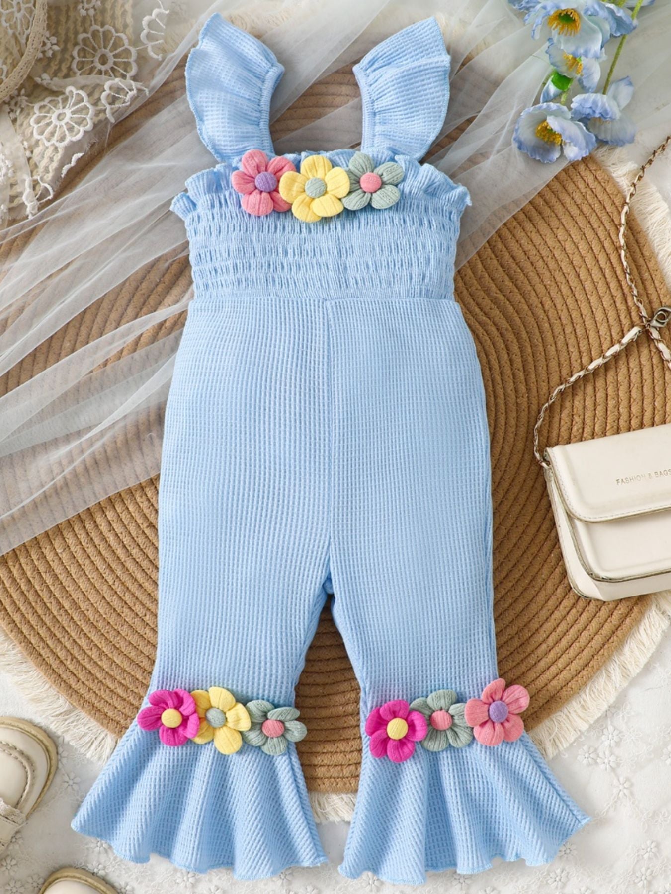 Baby blue cotton smocked jumpsuit with floral applique on bodice and flared legs.