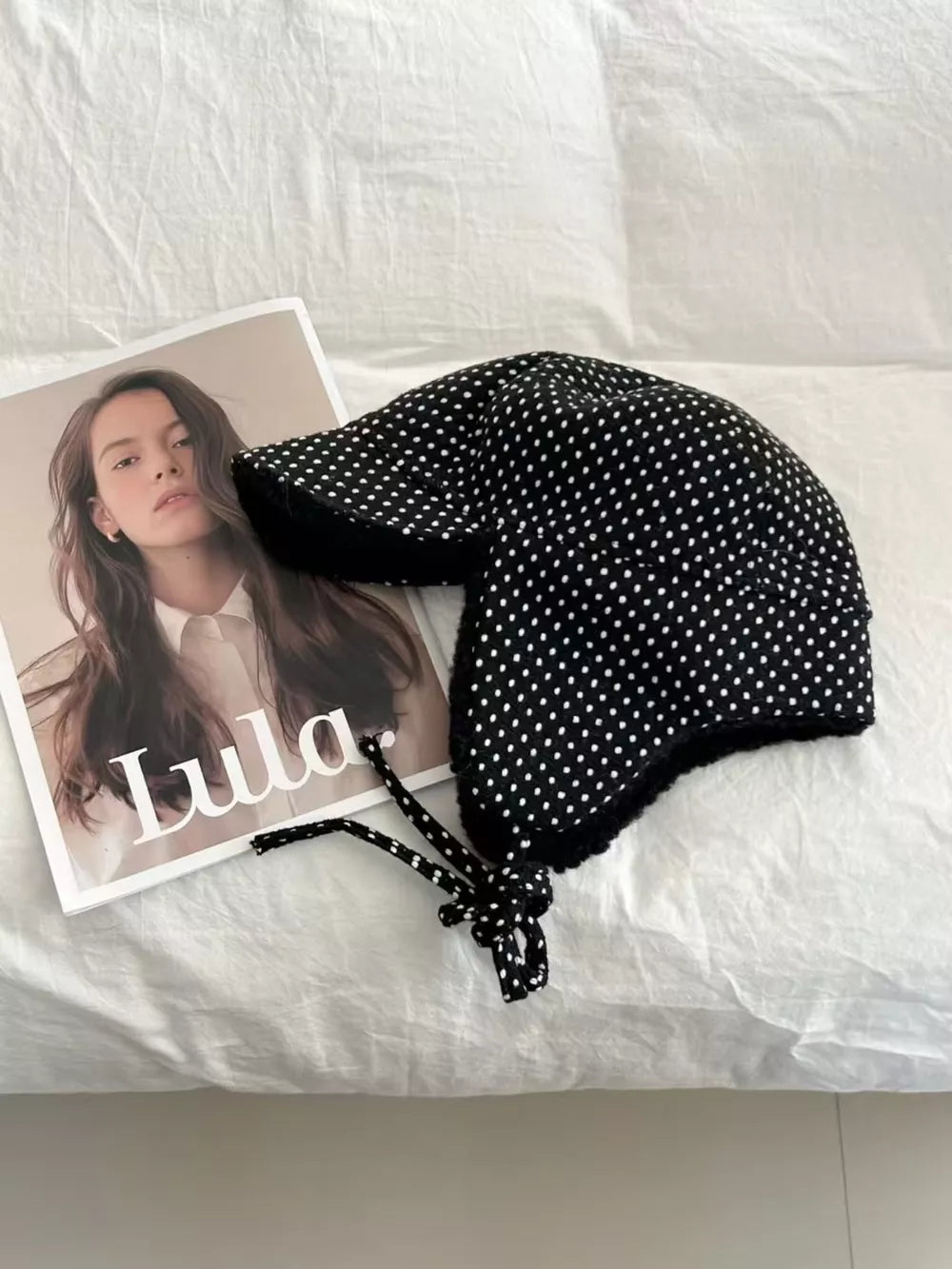 Black polka dot fleece hat with ear flaps and tie strings.