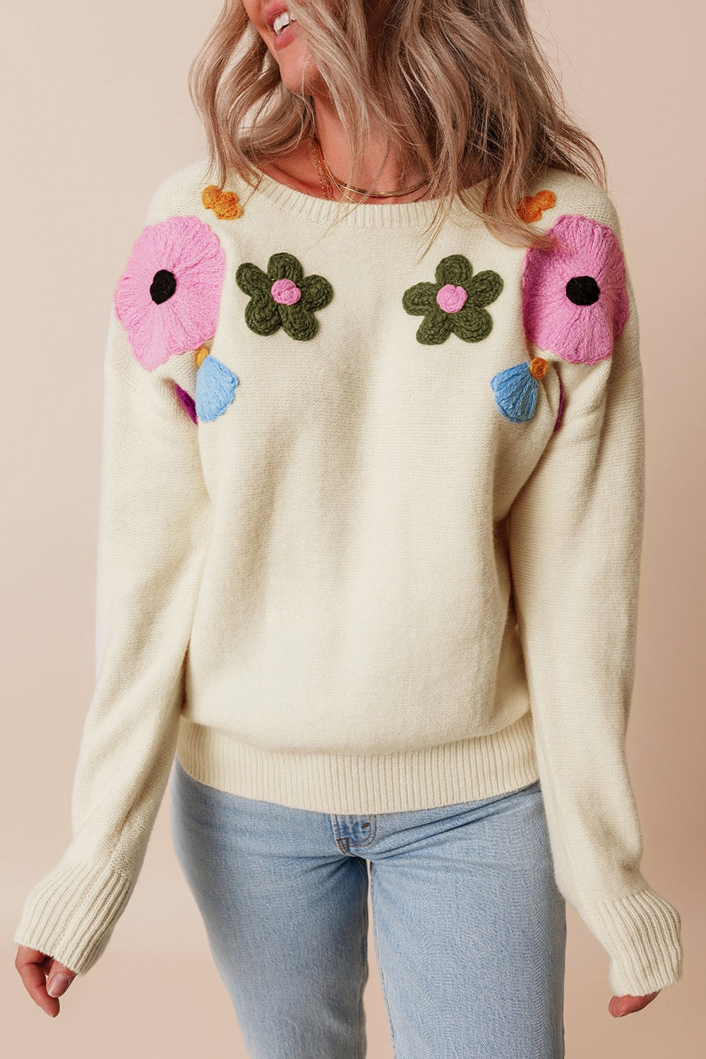 Cream knit sweater with embroidered floral appliqués and ribbed cuffs and hem.