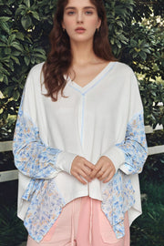 White waffle knit blouse with floral print sleeves and V-neckline.