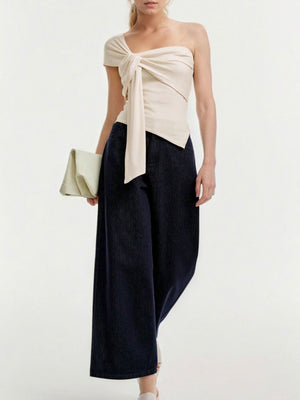 Beige asymmetrical t-shirt with knot detail and one short sleeve, worn by a woman.
