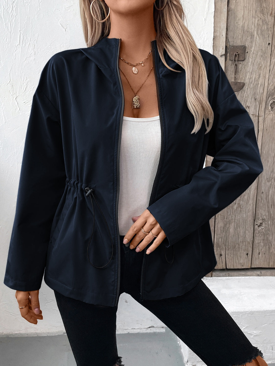 Navy utility jacket with cinched waistline and zip front, styled with a white tank top.