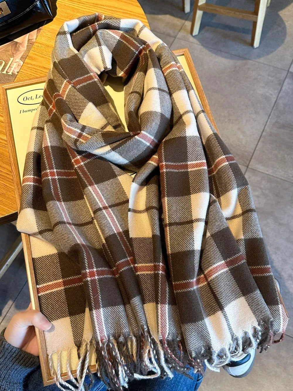 Plaid fringe scarf in taupe with white and red accents, featuring a cozy, heritage-inspired design.