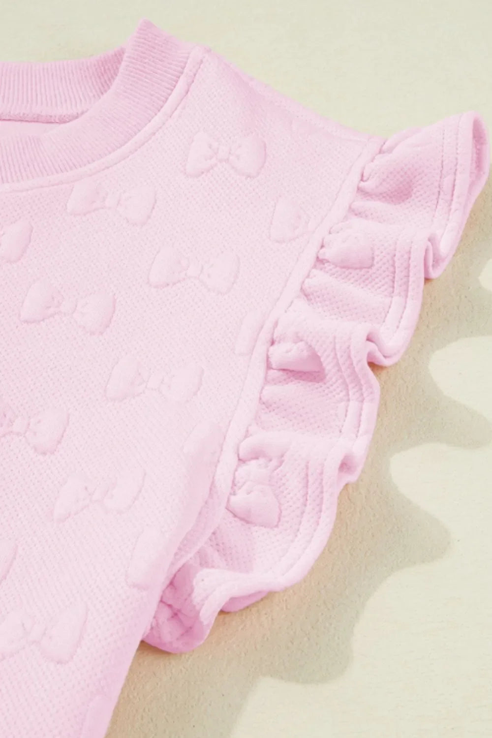 Blush pink loungewear set with embossed bow pattern and ruffle sleeves.
