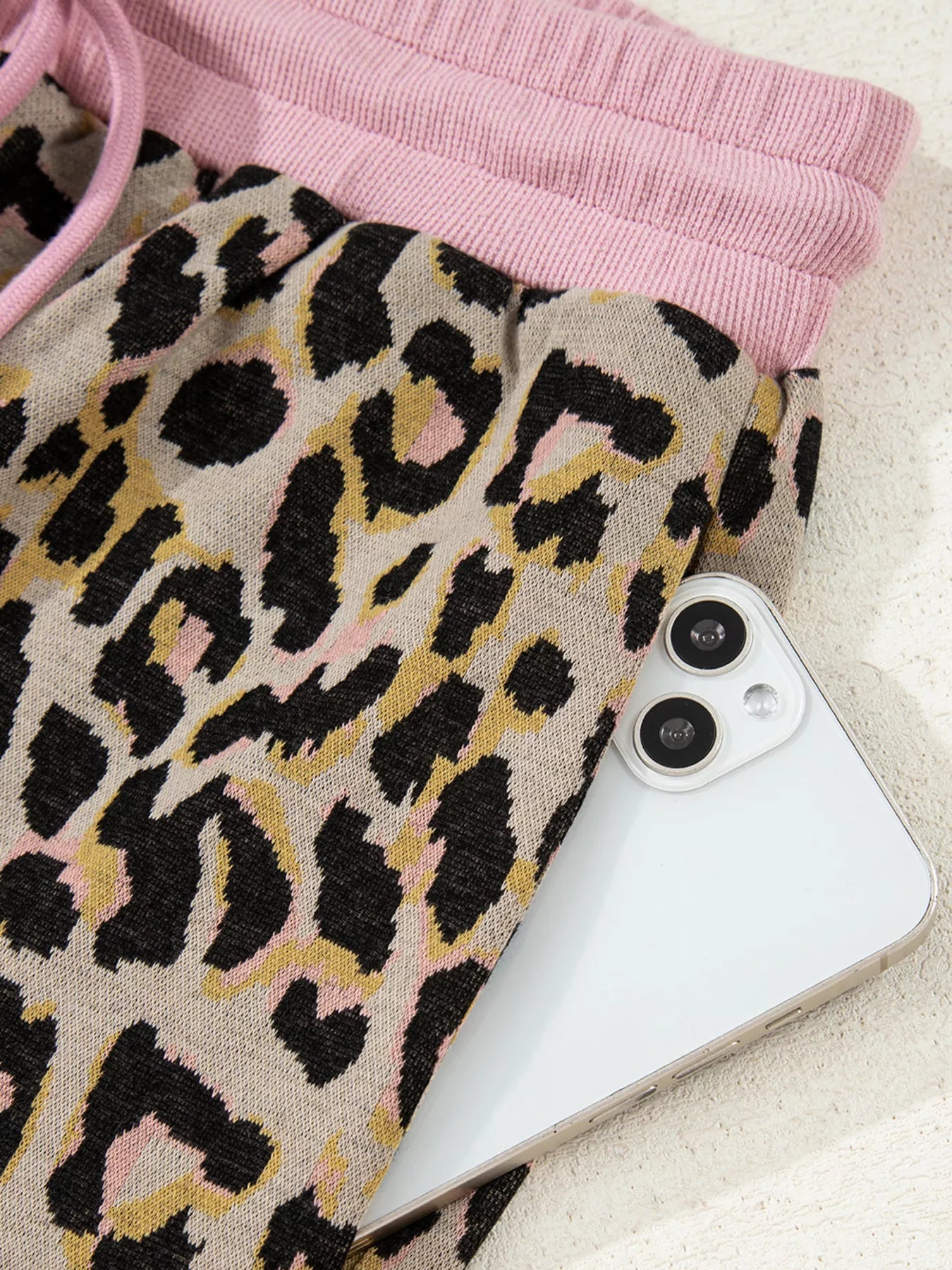 Leopard print loungewear pants with pink drawstring waist and side pocket holding a phone.