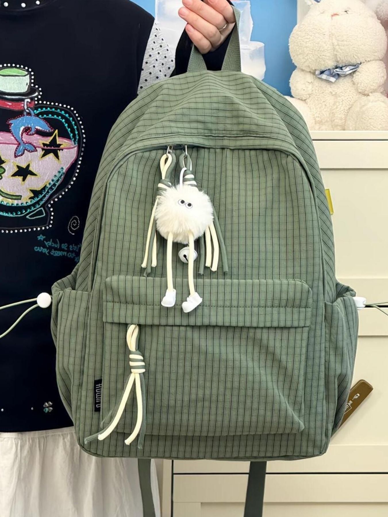 Green plaid nylon backpack with fuzzy charm and tassel details.