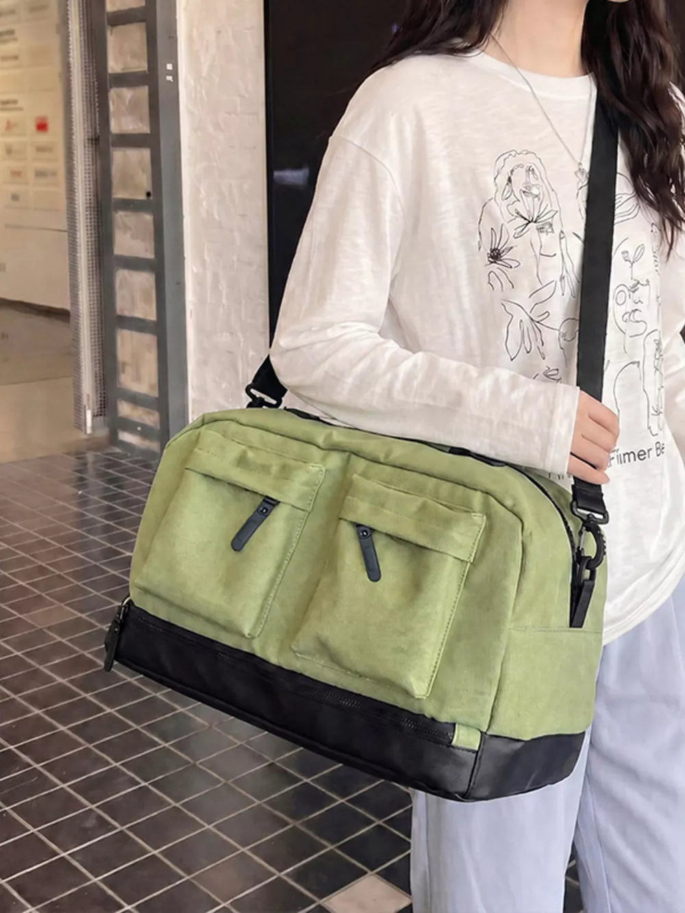 Green duffle bag with two front zip pockets and black trim, worn crossbody.