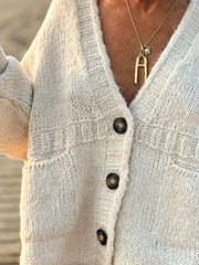 Beige bouclé knit cardigan with textured details, button front, and pockets.