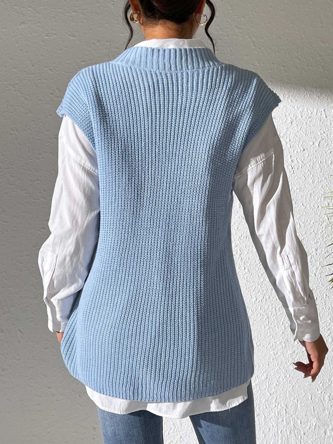 Light blue ribbed knit sleeveless vest with mock neck, styled over a white shirt.