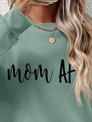 Sage green crewneck sweatshirt with black "mom At" graphic, crew neck, long sleeves, ribbed cuffs and hem.