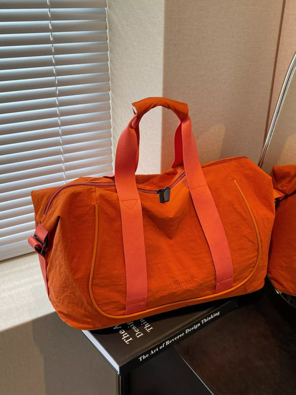 Orange lightweight Oxford cloth duffel bag with contrasting straps and embroidered logo detail.