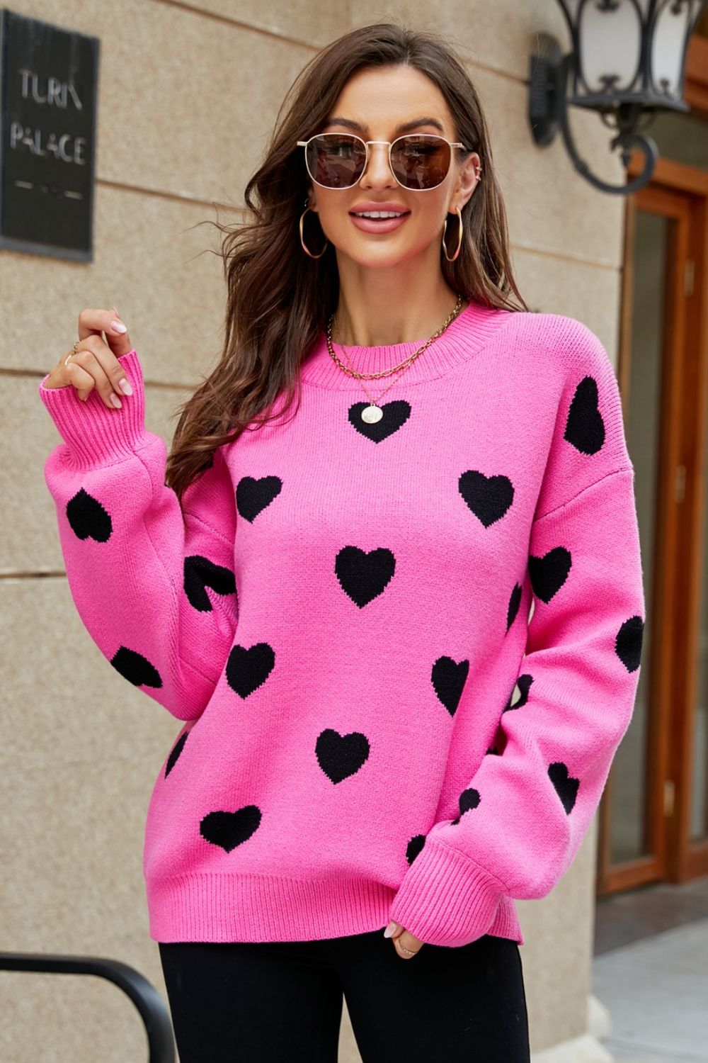 Pink knit sweater with black hearts, crew neck, and balloon sleeves.